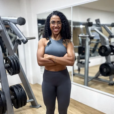 Kalianne Couto em uma academia, sorrindo e com os braços cruzados.